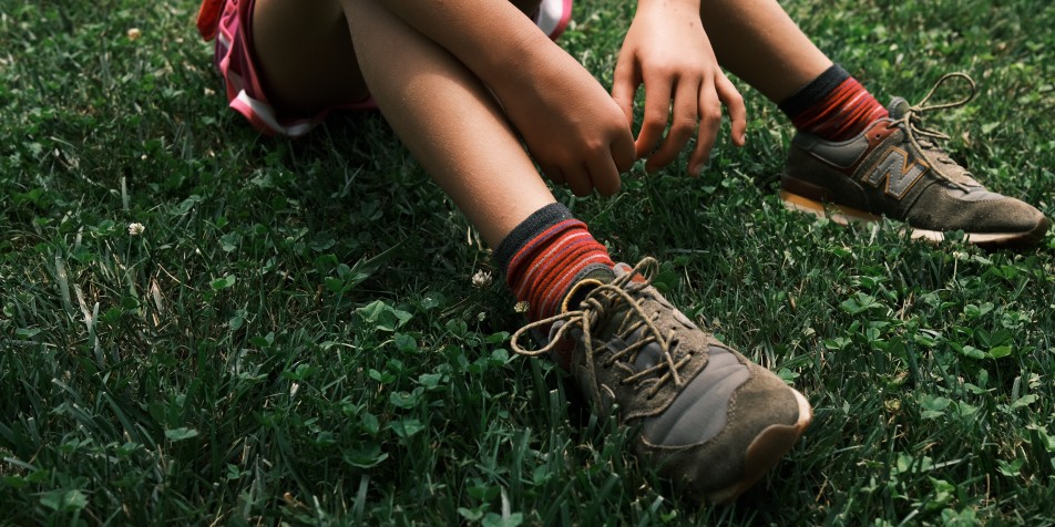 young person's knees and sneakers in grass 